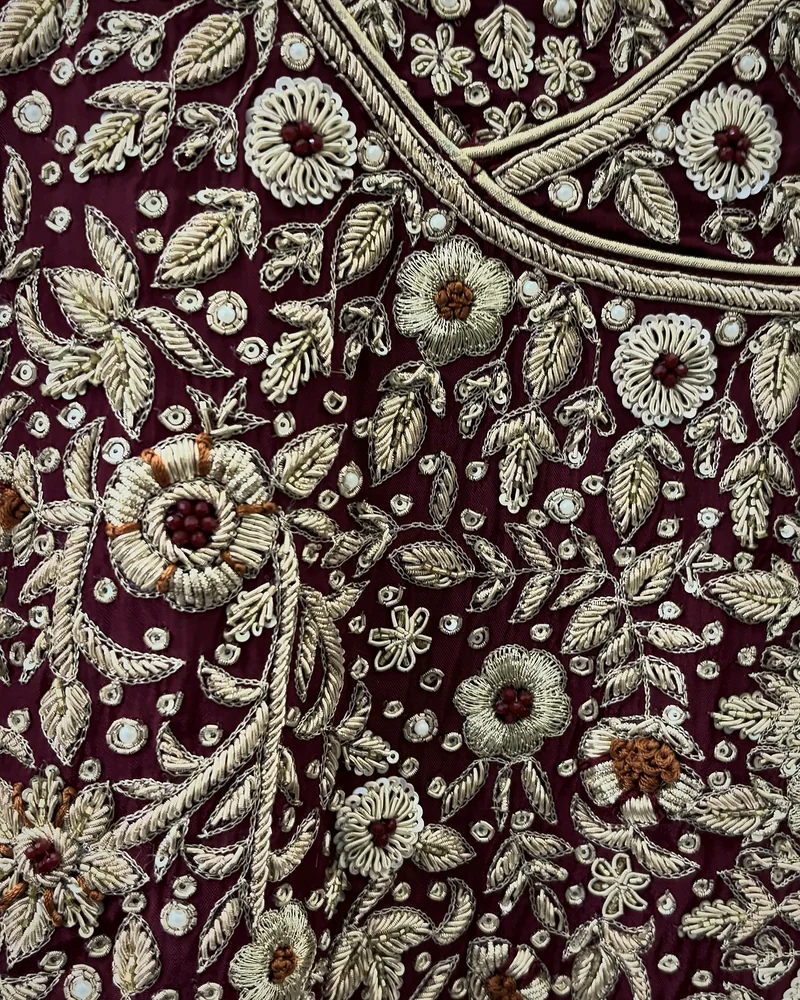 Close view of a bridal yoke on wine: raised dabka flowers with bead centres, dabka leaves and sequins